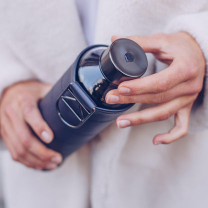 Een persoon in een lichte jas houdt een Equa - Waterfles - Mismatch Leather Graphite fles vast en schroeft met één hand de dop van de zwarte BPA-vrije Equa fles.