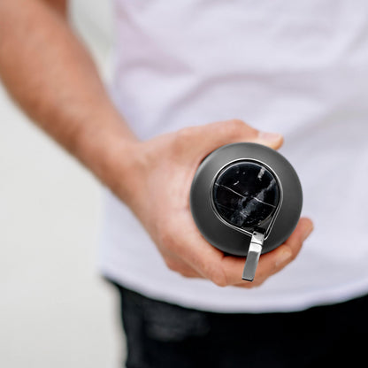 Een persoon die een Equa Thermo Stainless Steel Waterfles in Dark Grey vasthoudt, met een metalen handvat en een gebarsten deksel, van bovenaf gezien.