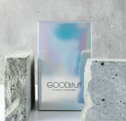 Een holografische doos met &quot;GOODstuff van Rainpharma&quot;, geplaatst tussen twee grijze betonblokken tegen een gestructureerde achtergrond, op de markt gebracht als een met collageen versterkt voedingssupplement.